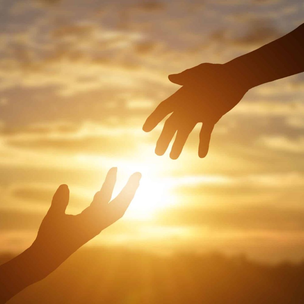 Silhouette of reaching, giving a helping hand, hope and support each other over sunset background.